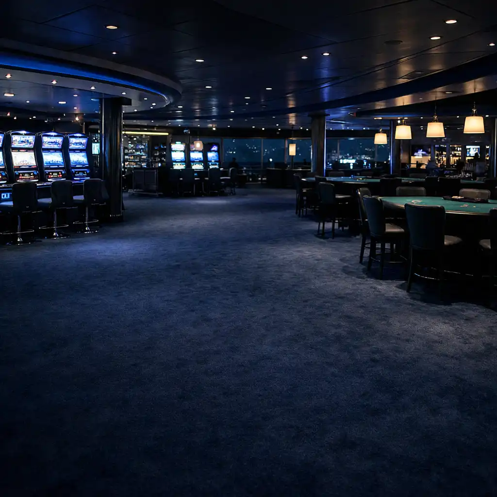 A wide-angle view of a modern cruise ship casino lounge at night, with slot machines and blackjack tables under cool blue lighting